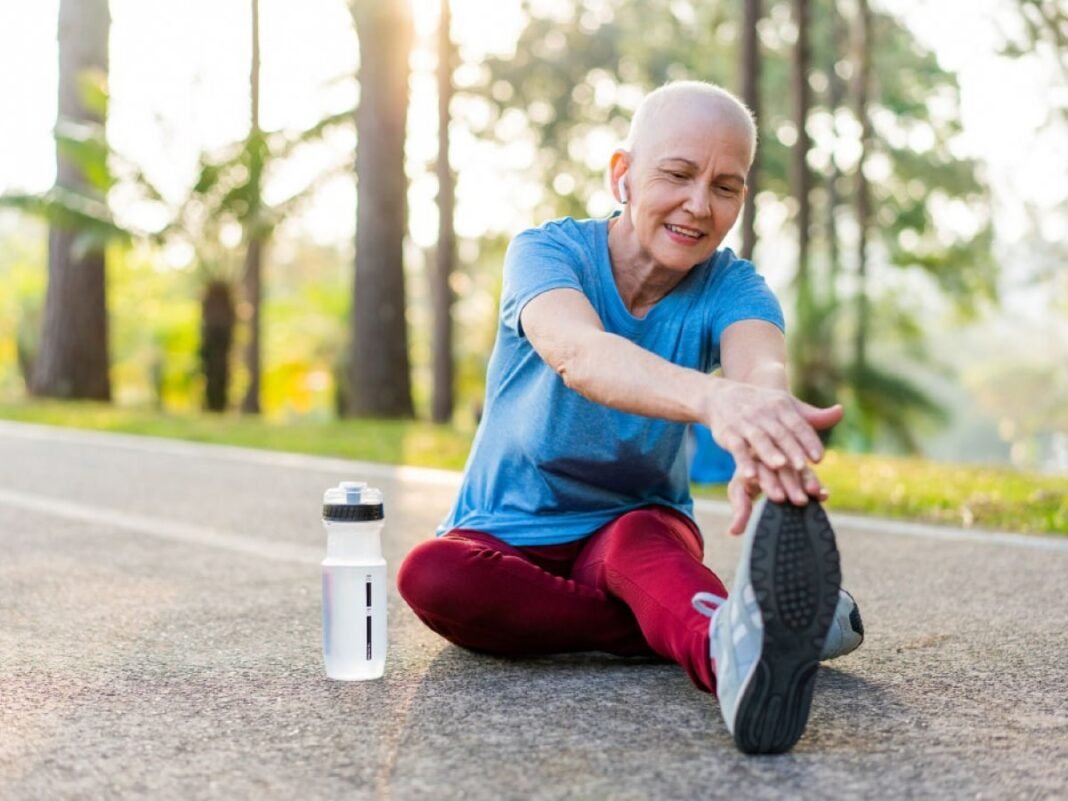 Breast cancer survivor with a shaved head stretching outdoors during exercise