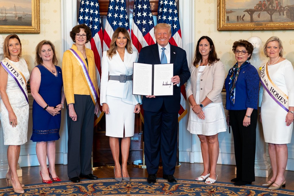 President Donald Trump signs the executive order creating a new women's health division at NIH, flanked by officials at the White House event.